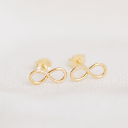 Minimal gold infinity symbol stud earrings close up on white background
