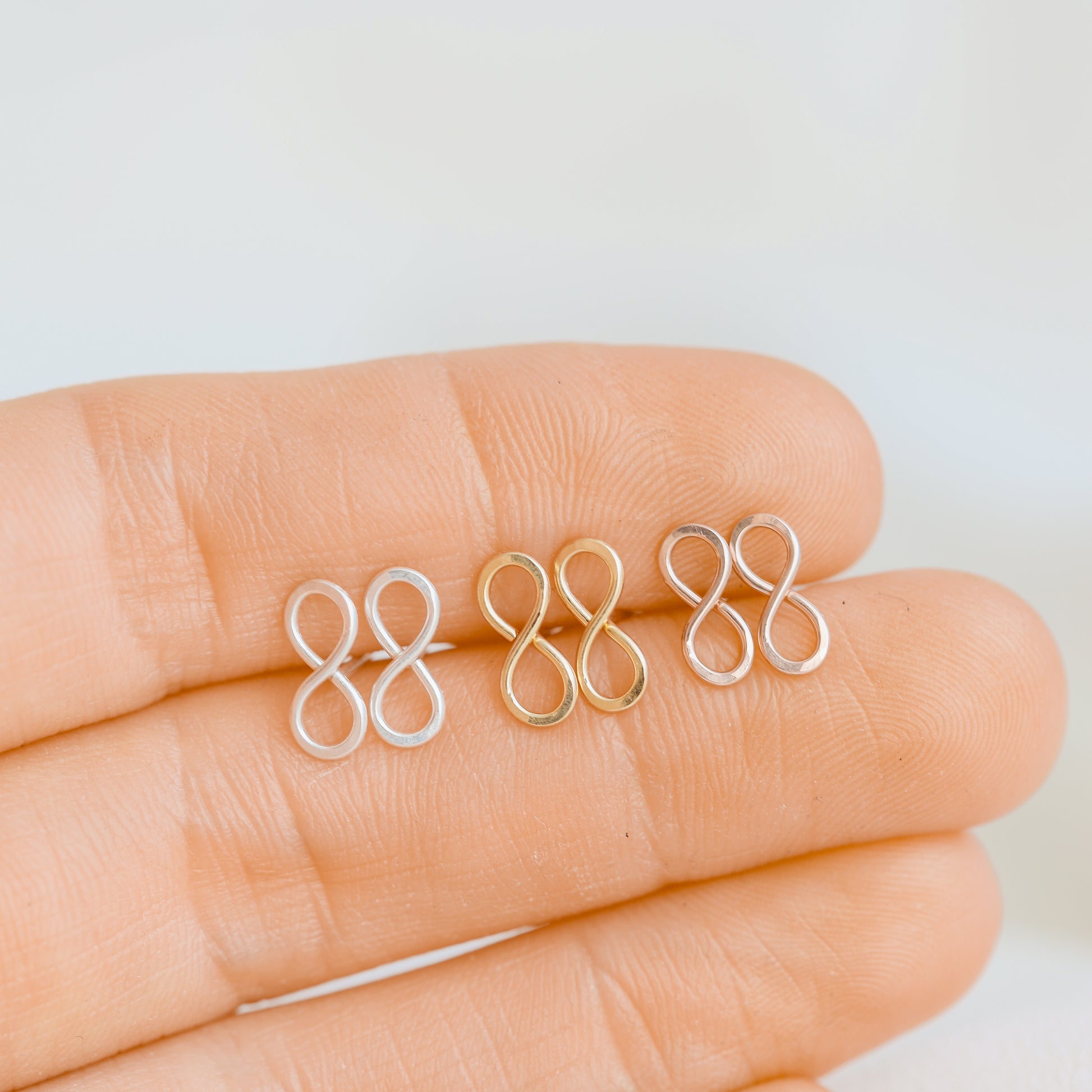 Small infinity symbol earrings shown on fingers for size reference
