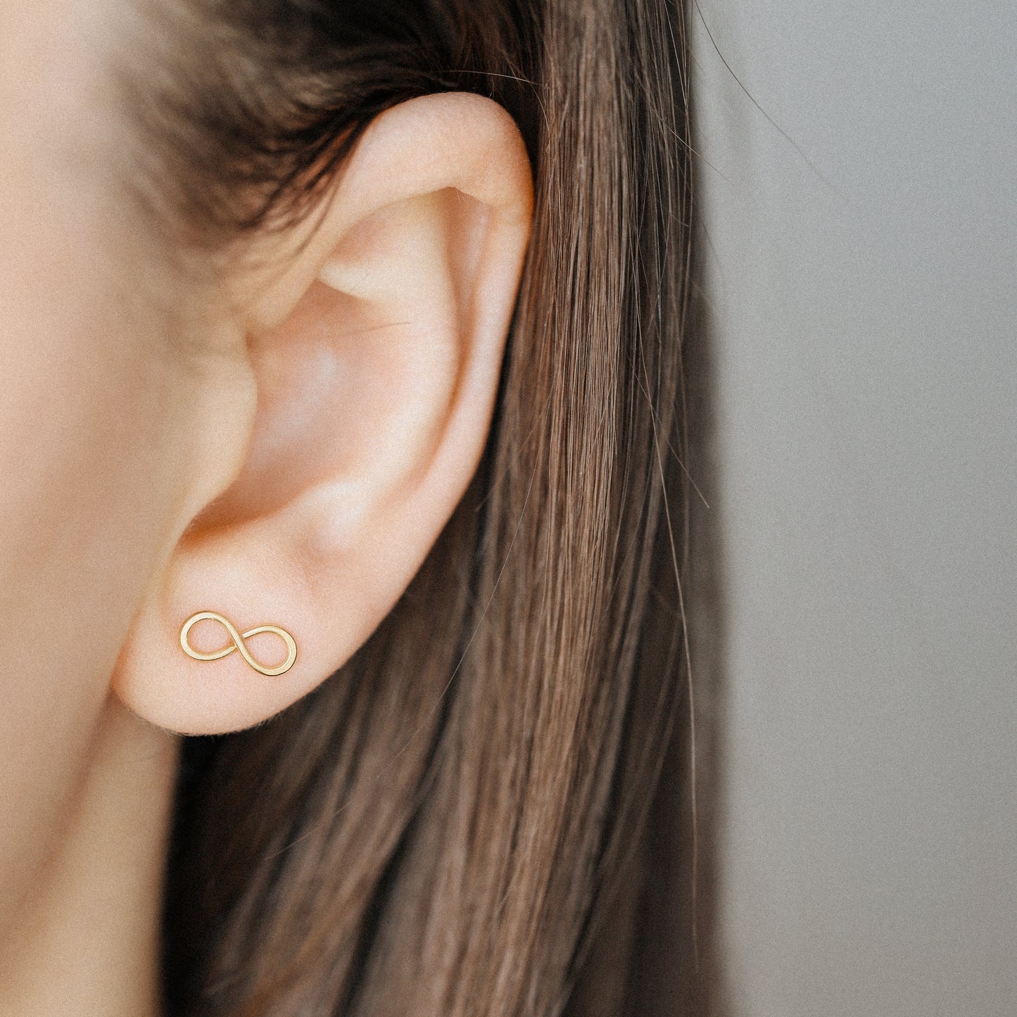 Gold infinity stud earrings worn on ear minimalist everyday look