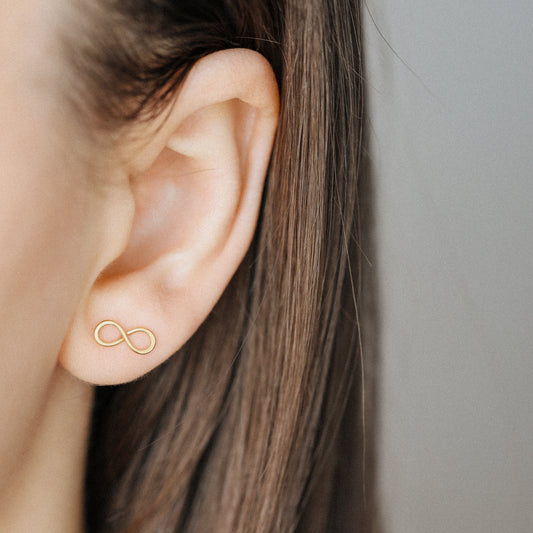 Gold infinity stud earrings worn on ear minimalist everyday look