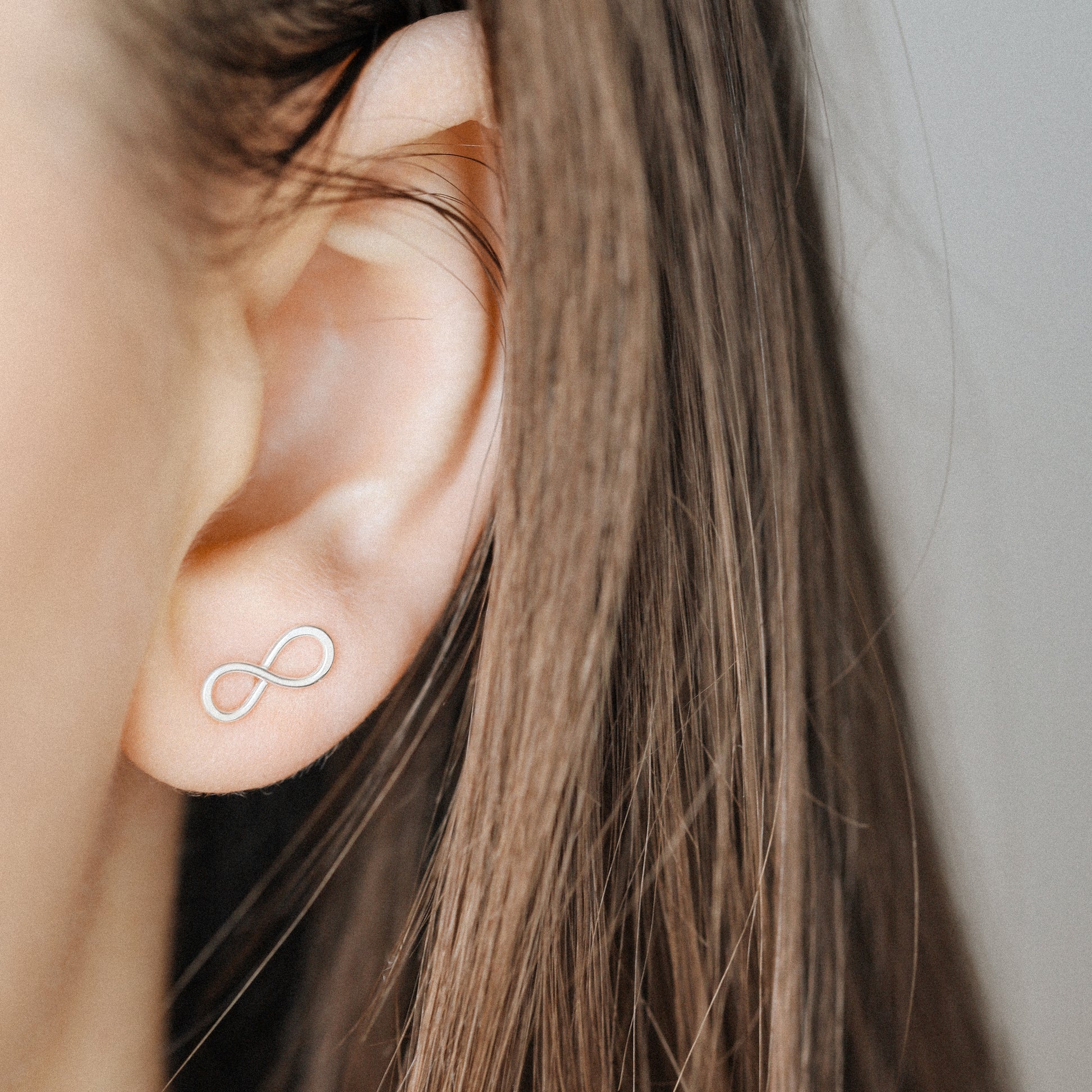 Sterling silver infinity symbol earrings worn on ear close up