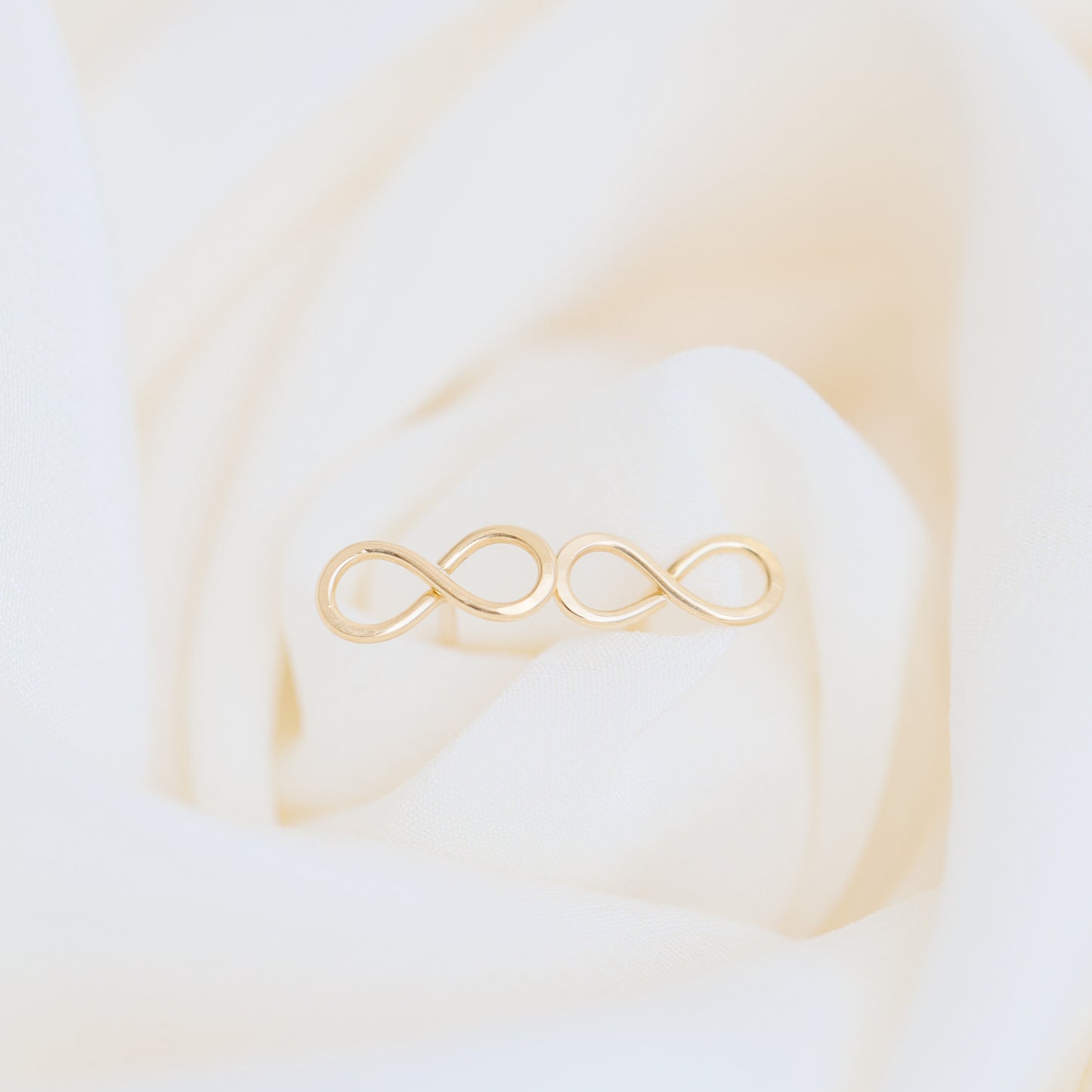 Dainty infinity stud earrings in gold on elegant fabric background