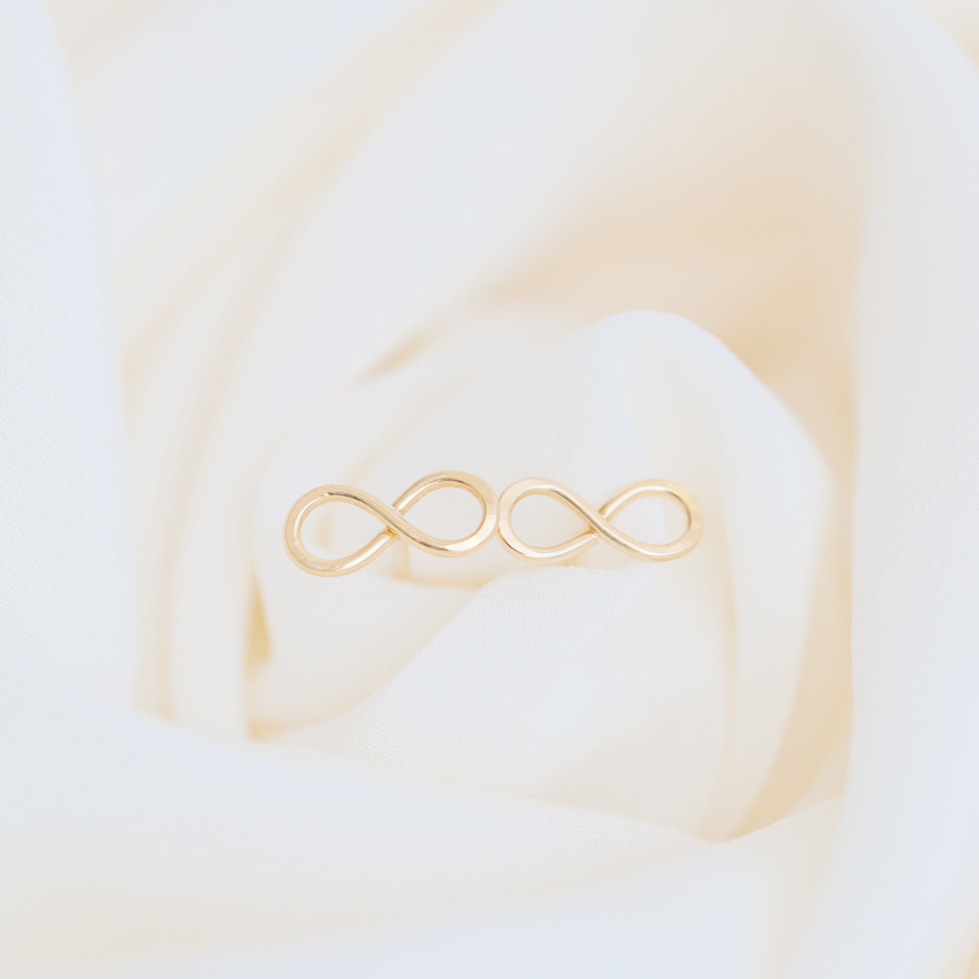 Dainty infinity stud earrings in gold on elegant fabric background