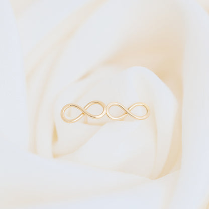 Dainty infinity stud earrings in gold on elegant fabric background