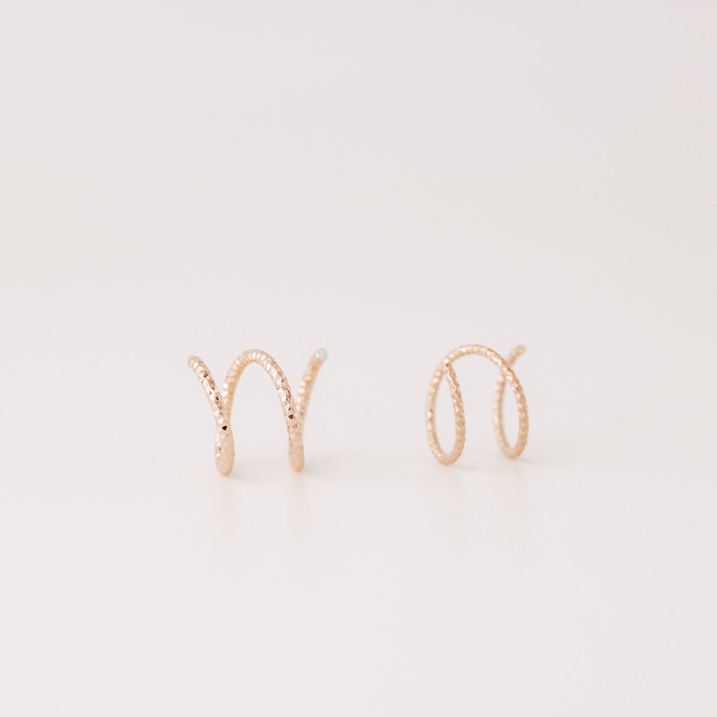 Close-up of a woman's ear wearing tiny rose gold double hoop illusion earrings with a diamond-cut texture, designed to create the appearance of two piercings with a single hole.