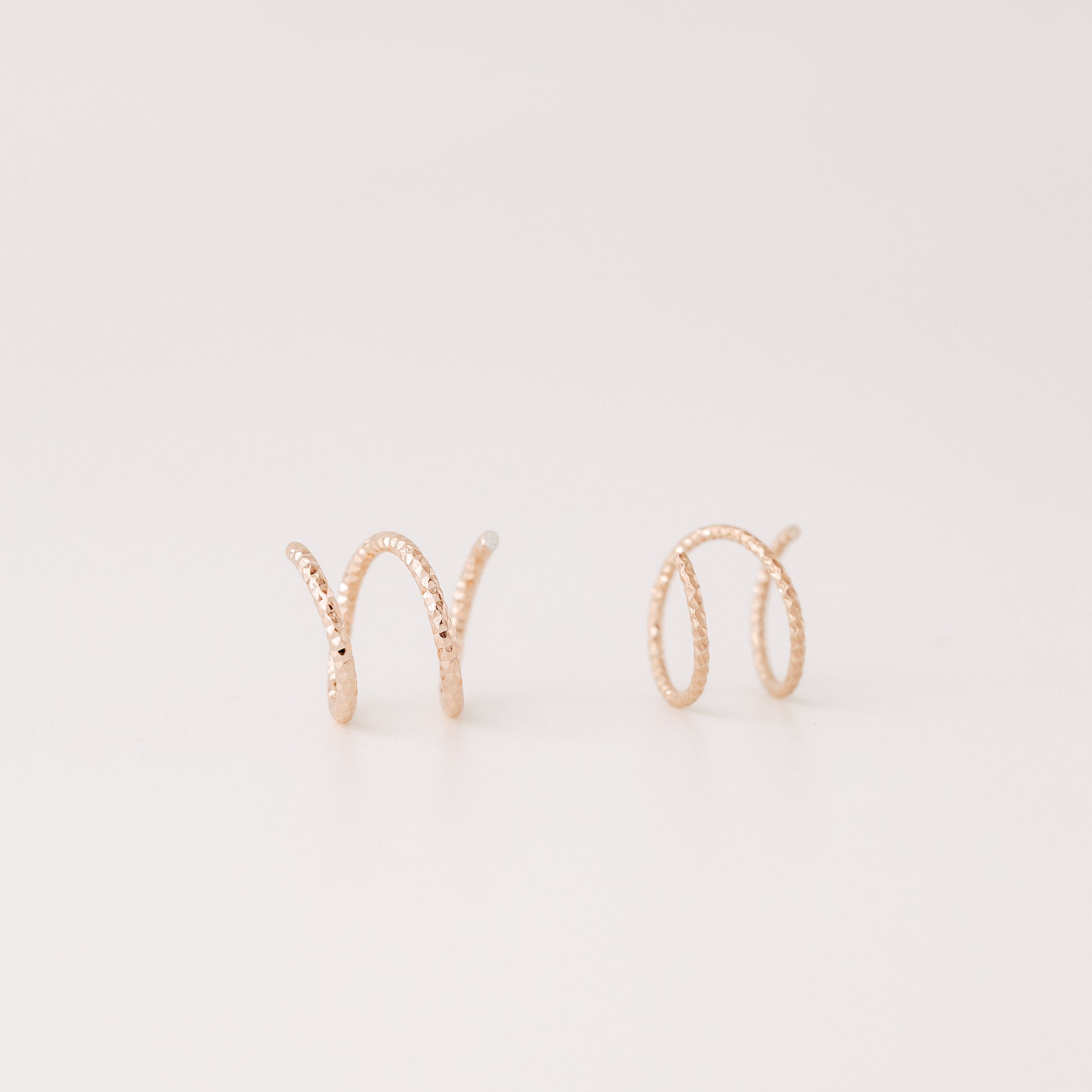 Close-up of a woman's ear wearing tiny rose gold double hoop illusion earrings with a diamond-cut texture, designed to create the appearance of two piercings with a single hole.