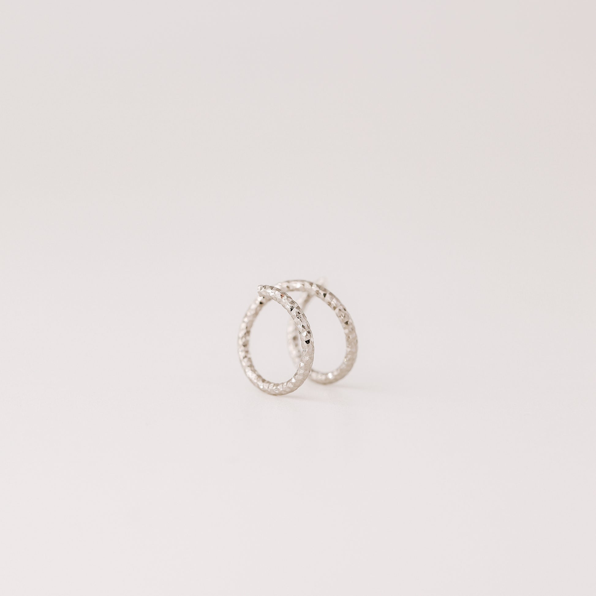 Minimal black double hoop spiral earrings worn on ear, tiny ruthenium sterling silver illusion hoops creating double piercing look, diamond cut texture close-up