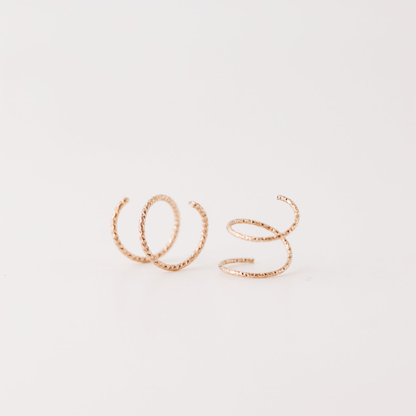 Close-up of a woman's ear wearing tiny rose gold double hoop illusion earrings with a diamond-cut texture, designed to create the appearance of two piercings with a single hole.