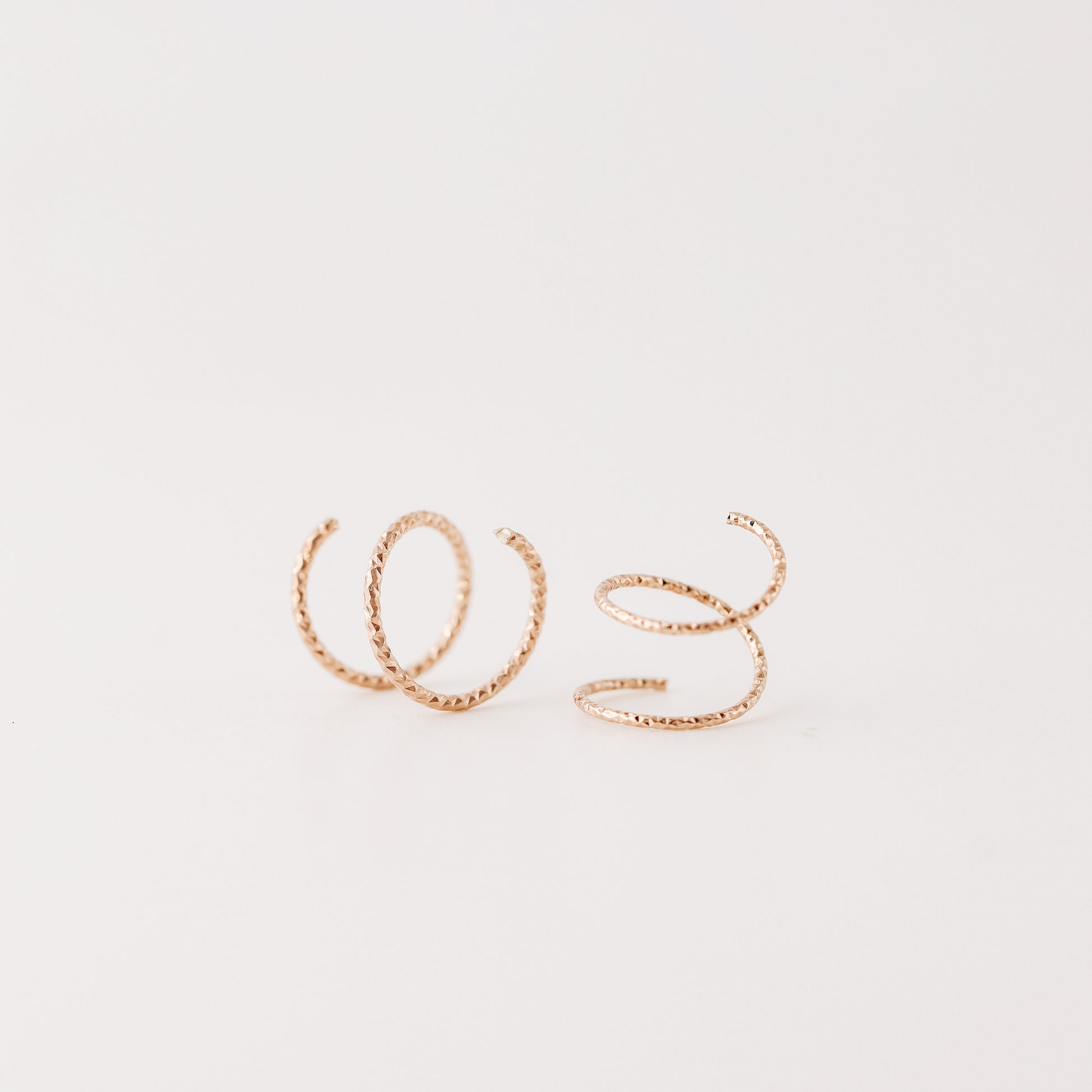 Close-up of a woman's ear wearing tiny rose gold double hoop illusion earrings with a diamond-cut texture, designed to create the appearance of two piercings with a single hole.