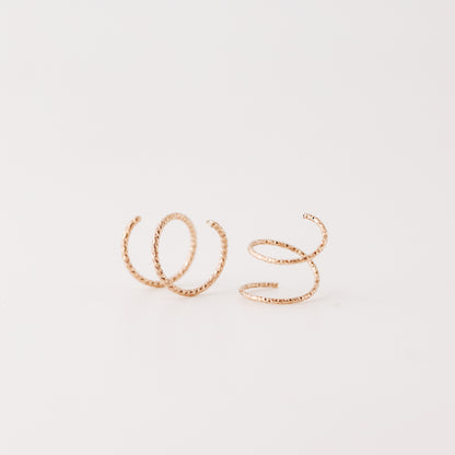 Close-up of a woman's ear wearing tiny rose gold double hoop illusion earrings with a diamond-cut texture, designed to create the appearance of two piercings with a single hole.
