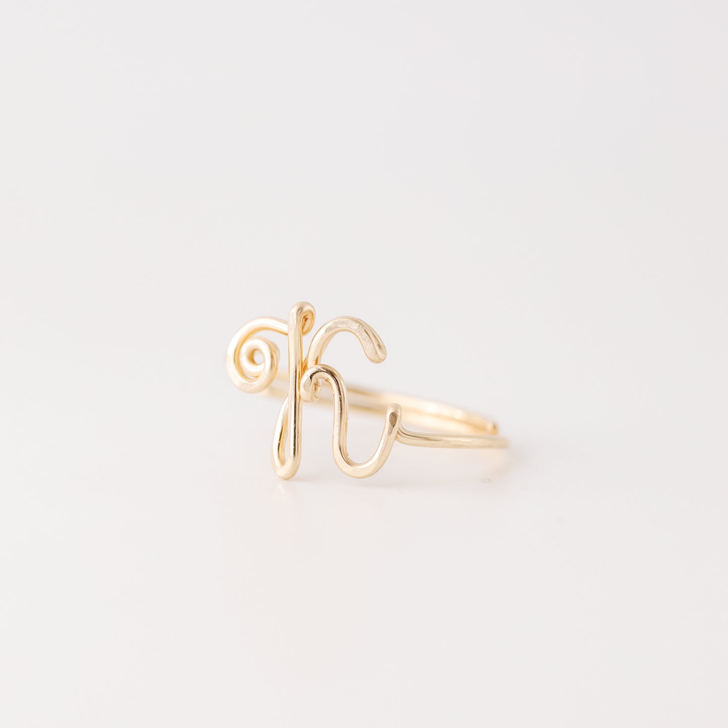 Handmade uppercase cursive letter K wire ring in polished gold, shown from a side view on a clean white background.