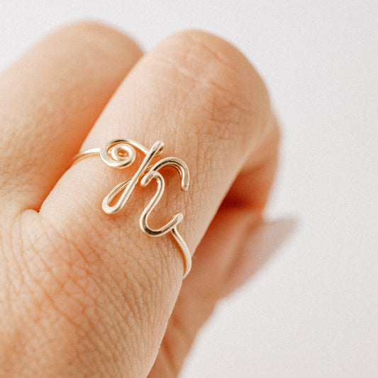 Handmade gold wire ring featuring a bold uppercase cursive letter K, worn on a hand against a light background.