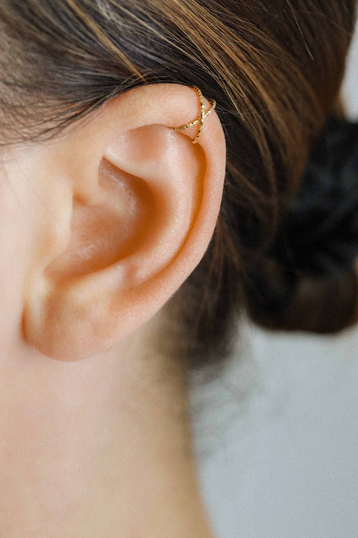 Close-up of a person's ear wearing a textured gold criss-cross ear cuff on the helix, handmade adjustable jewelry without piercing.