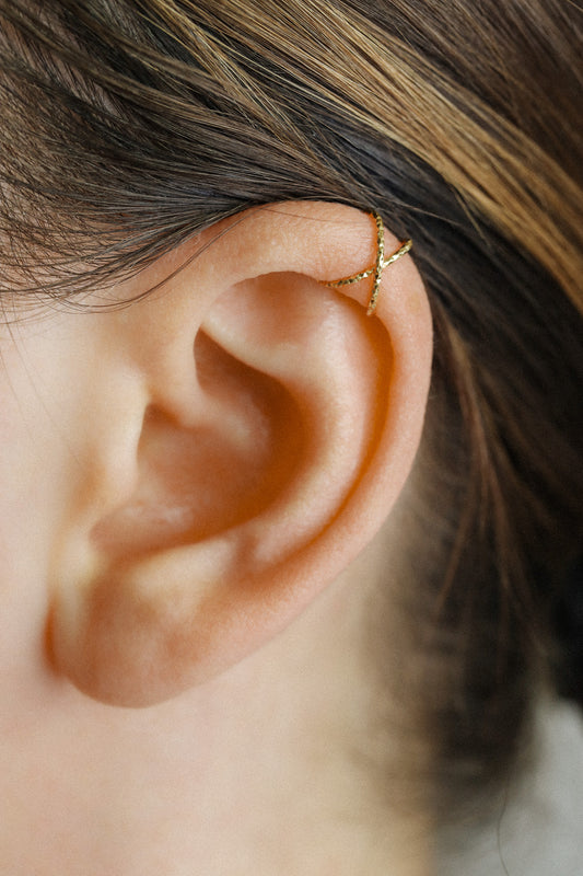 Close-up of a person's ear wearing a textured gold criss-cross ear cuff on the helix, handmade adjustable jewelry without piercing.