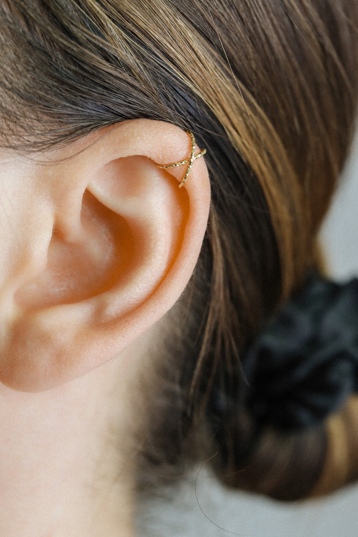 Close-up of a person's ear wearing a textured gold criss-cross ear cuff on the helix, handmade adjustable jewelry without piercing.