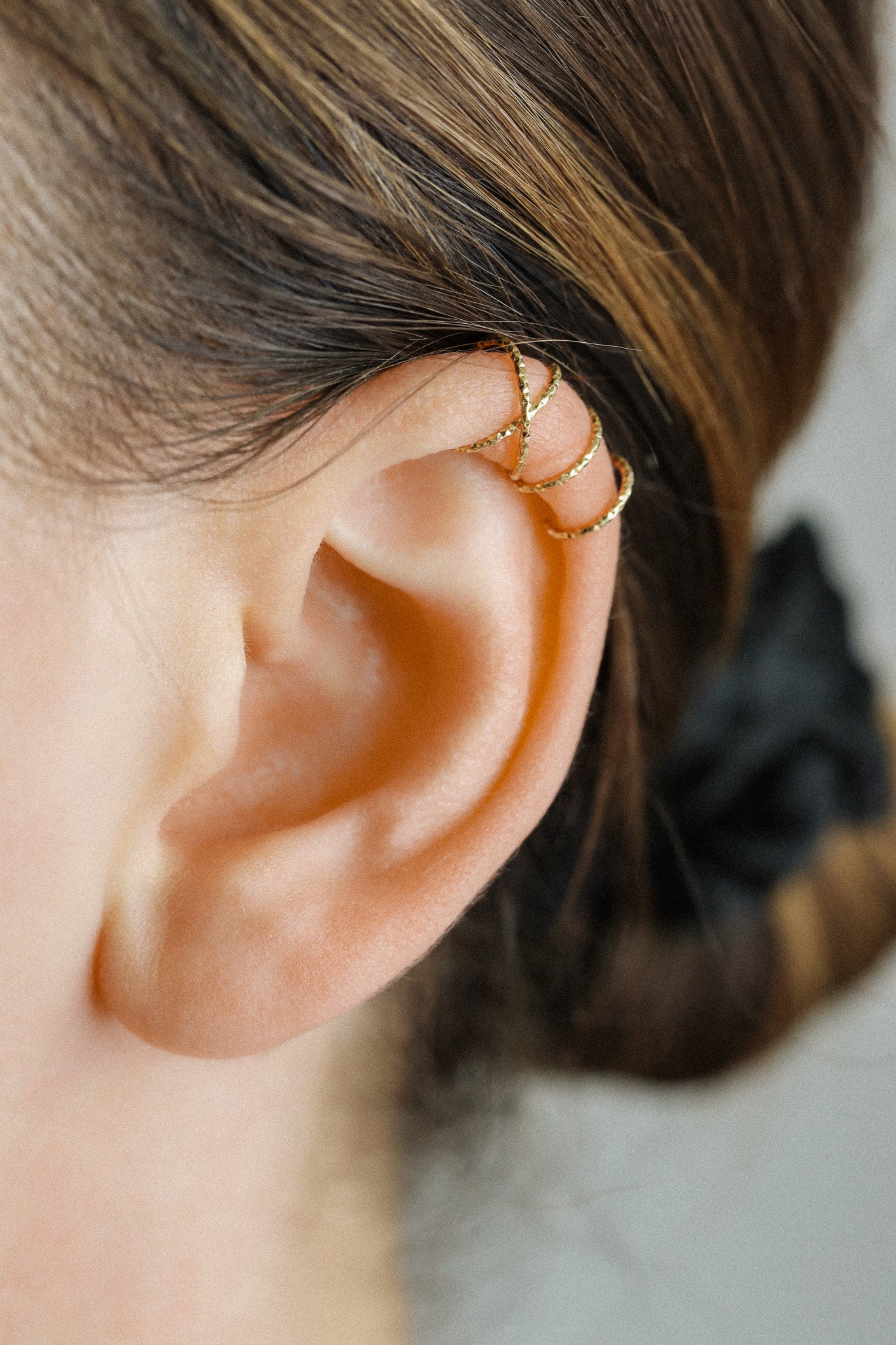 Close-up of a person's ear wearing a textured gold criss-cross ear cuff on the helix, handmade adjustable jewelry without piercing.