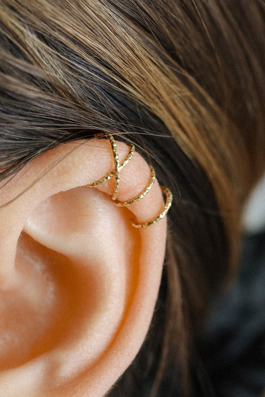 Close-up of a person's ear wearing a textured gold criss-cross ear cuff on the helix, handmade adjustable jewelry without piercing.