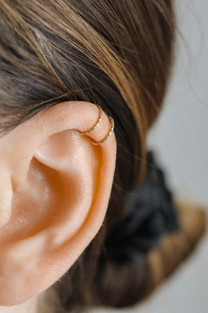 Close-up of a person's ear wearing a textured gold criss-cross ear cuff on the helix, handmade adjustable jewelry without piercing.