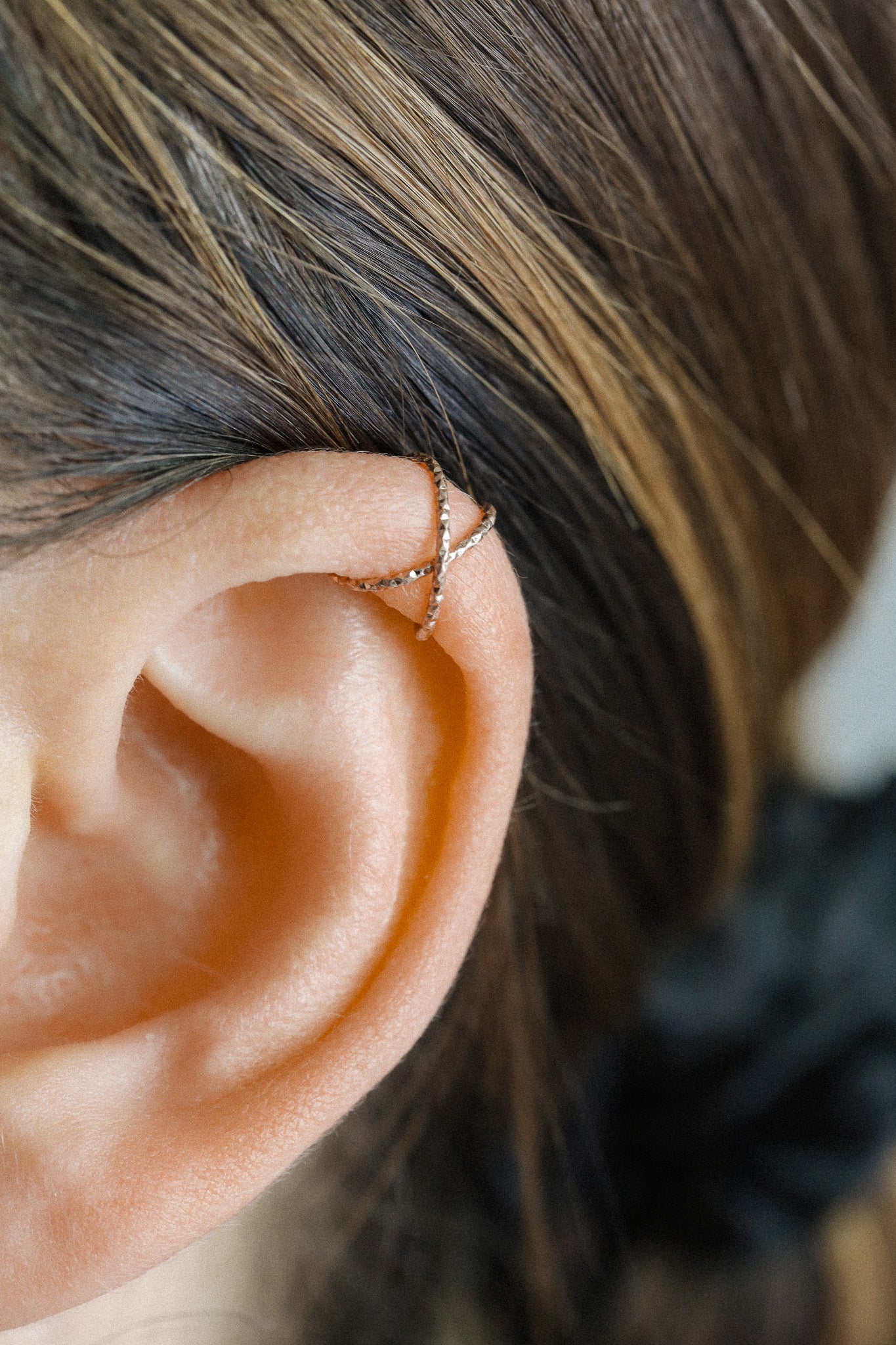 Close-up of a person wearing a rose gold criss-cross textured ear cuff on the helix, handmade adjustable faux piercing jewelry.