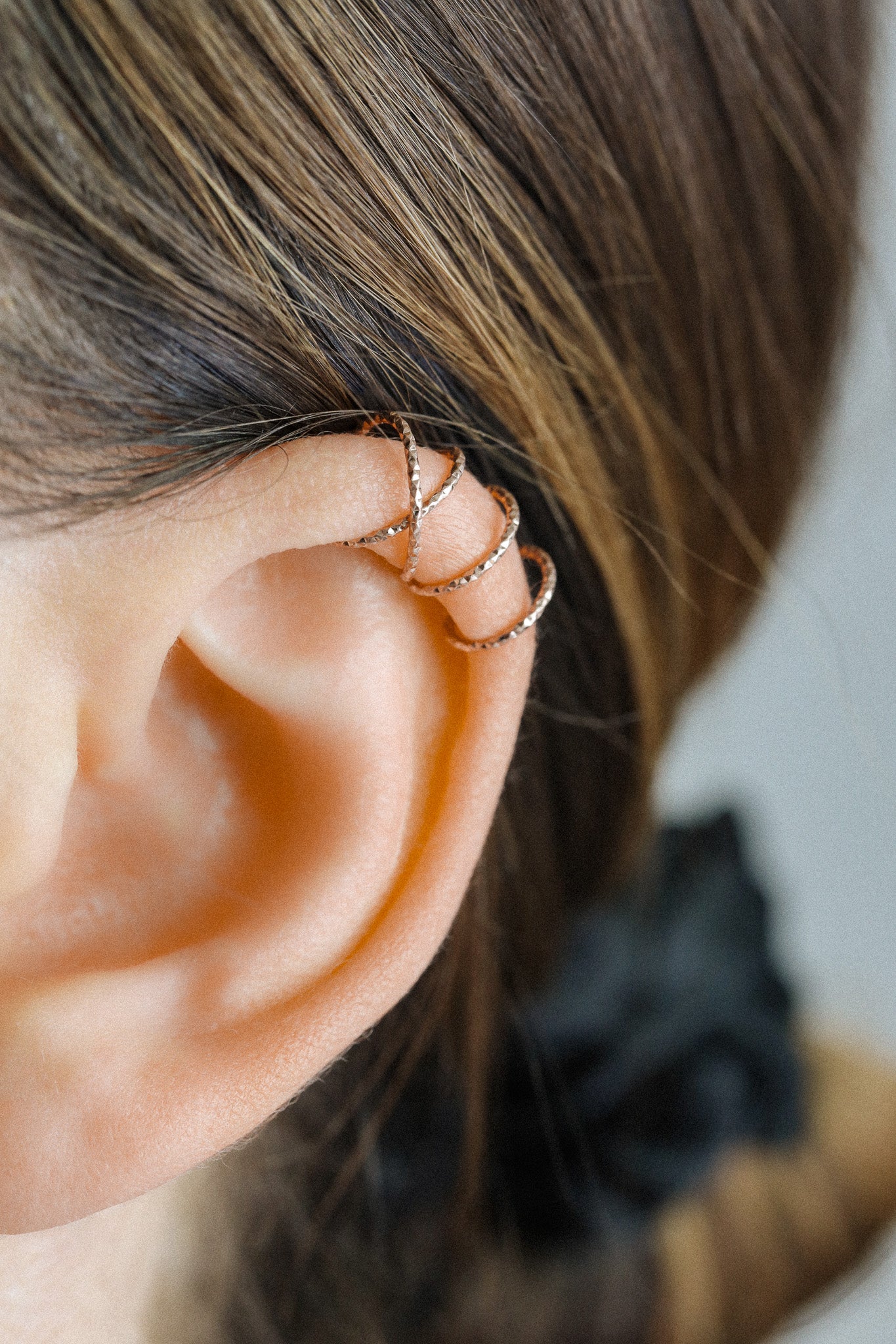 Close-up of a person wearing a rose gold criss-cross textured ear cuff on the helix, handmade adjustable faux piercing jewelry.
