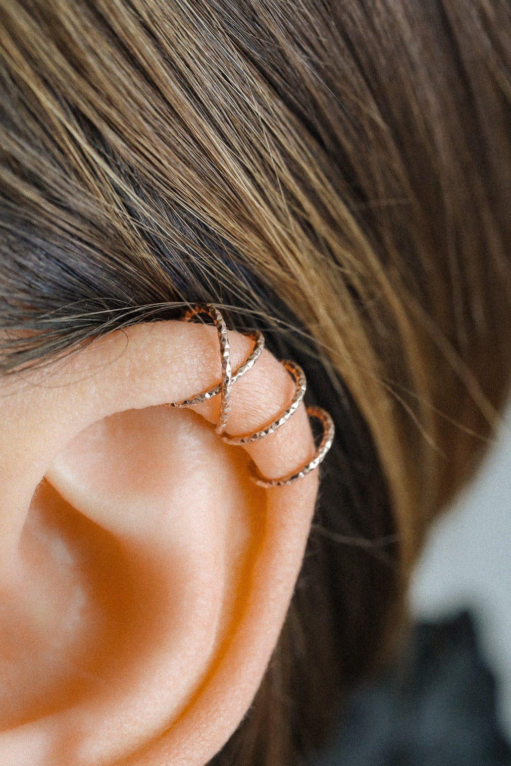 Close-up of a person wearing a rose gold criss-cross textured ear cuff on the helix, handmade adjustable faux piercing jewelry.