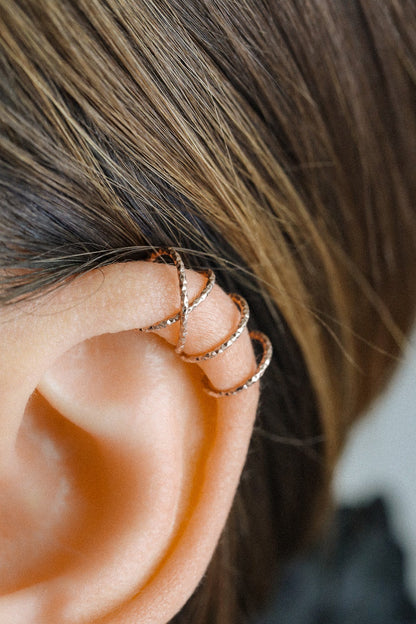 Close-up of a person wearing a rose gold criss-cross textured ear cuff on the helix, handmade adjustable faux piercing jewelry.