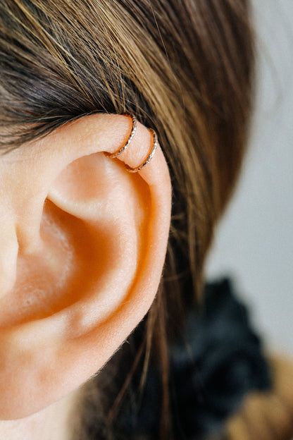 Close-up of a person wearing a rose gold criss-cross textured ear cuff on the helix, handmade adjustable faux piercing jewelry.