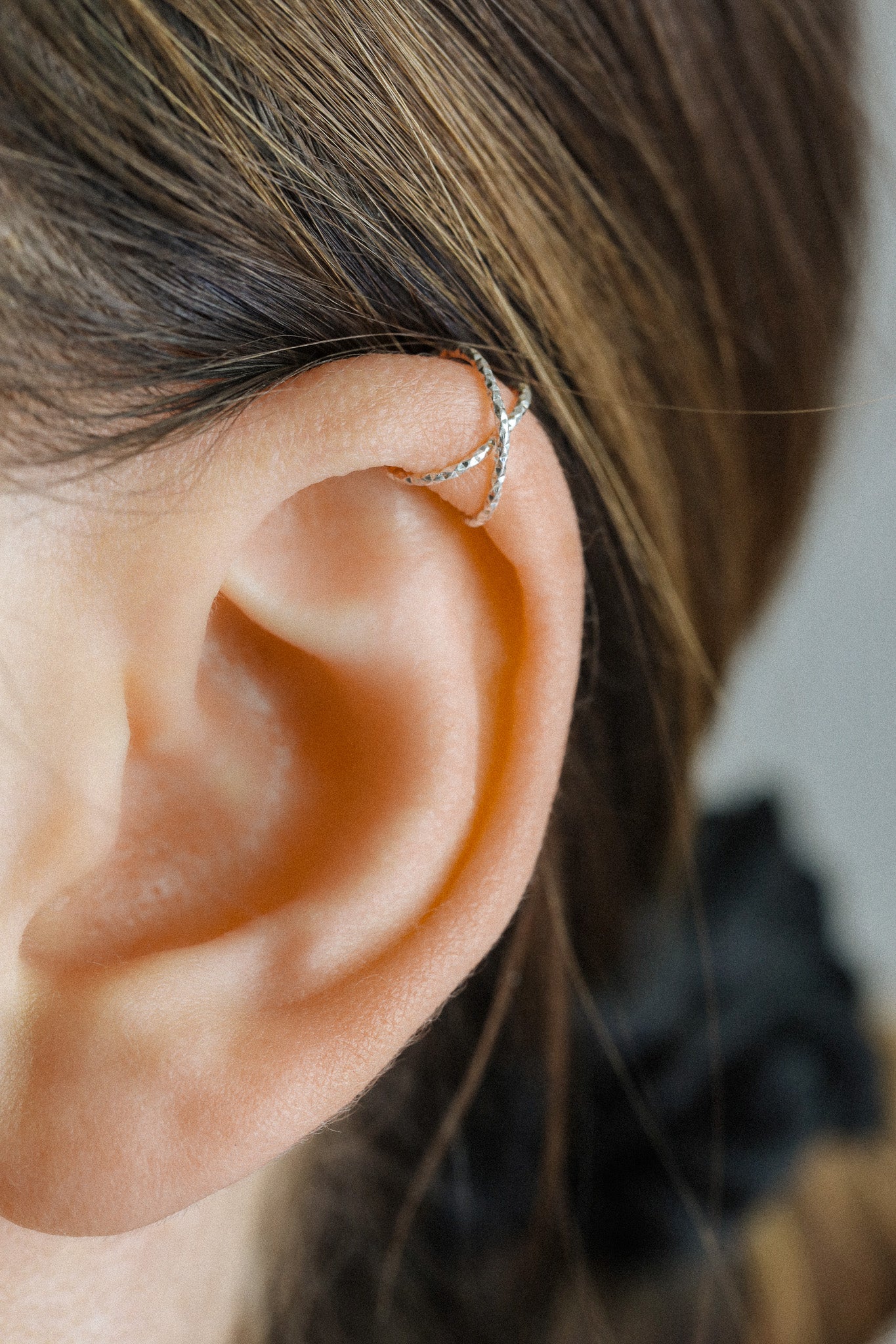 Close-up profile of a person's ear wearing a textured silver criss-cross ear cuff on the helix, handmade from diamond-cut 925 sterling silver.