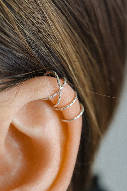 Close-up profile of a person's ear wearing a textured silver criss-cross ear cuff on the helix, handmade from diamond-cut 925 sterling silver.