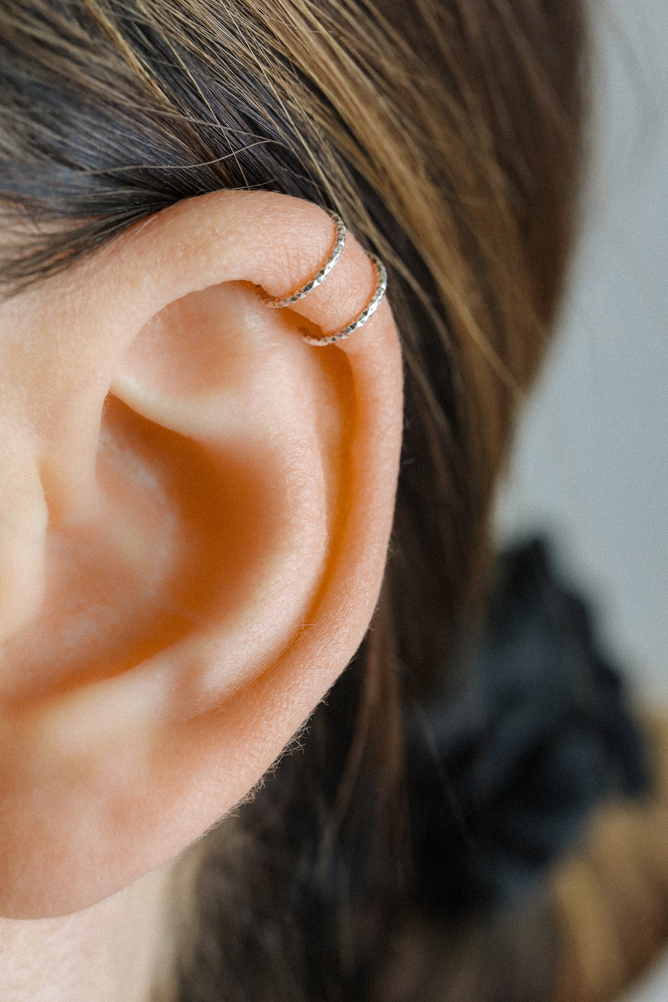 Close-up profile of a person's ear wearing a textured silver criss-cross ear cuff on the helix, handmade from diamond-cut 925 sterling silver.