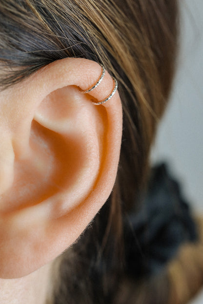 Close-up profile of a person's ear wearing a textured silver criss-cross ear cuff on the helix, handmade from diamond-cut 925 sterling silver.