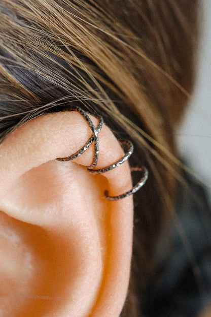 Close-up of a person wearing a textured black ruthenium criss-cross ear cuff and a double hoop cuff on the upper helix, handmade jewelry without piercing.