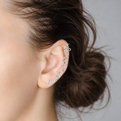 Personalized silver name ear climber handmade in flowing script, following the curve of the ear from the lobe upward, shown with a soft brown low bun hairstyle.