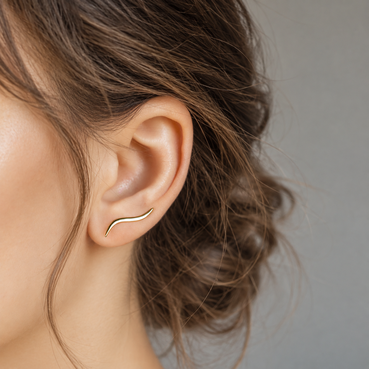 Polished gold wave ear climber worn diagonally across the lobe, showing the smooth sculptural curve and minimalist shape designed for one standard ear piercing.