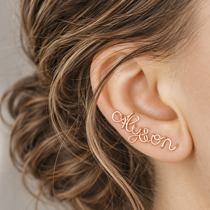 Handmade personalized name ear climber worn across the lobe through one standard piercing, featuring a custom flowing wire script design made with the chosen name or word up to 10 characters, available as a single left ear climber, single right ear climber or pair in solid 925 sterling silver, 14k gold filled and 14k rose gold filled.