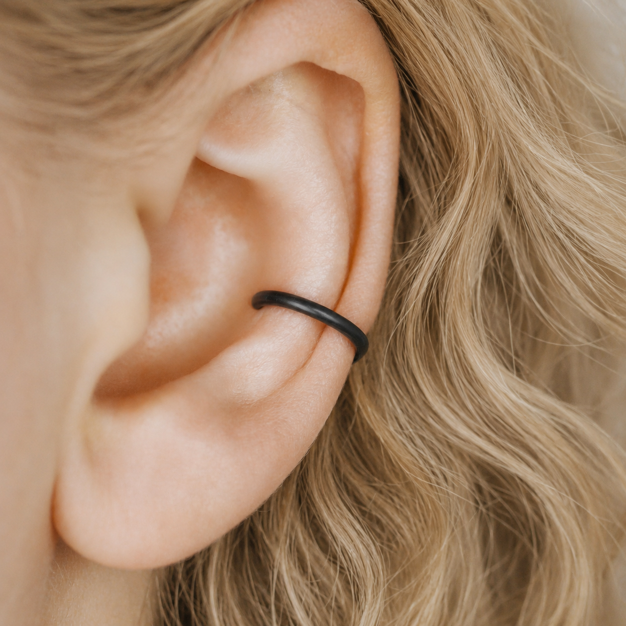 Thick smooth no-piercing ear cuff shown worn on different areas of the ear, including lobe, conch, cartilage and upper helix, with a rounded wrap design available in sterling silver, 18k yellow gold plated sterling silver, 18k rose gold plated sterling silver and black aluminum.