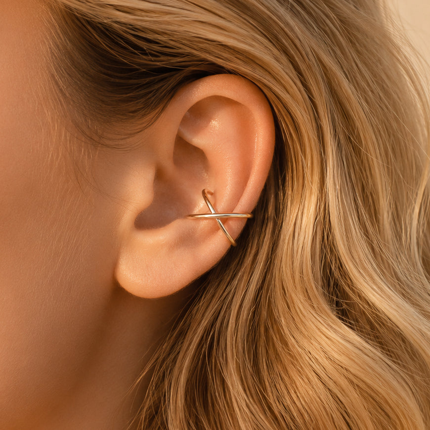 gold criss cross ear cuff worn on the upper ear, featuring a smooth minimalist no piercing design.