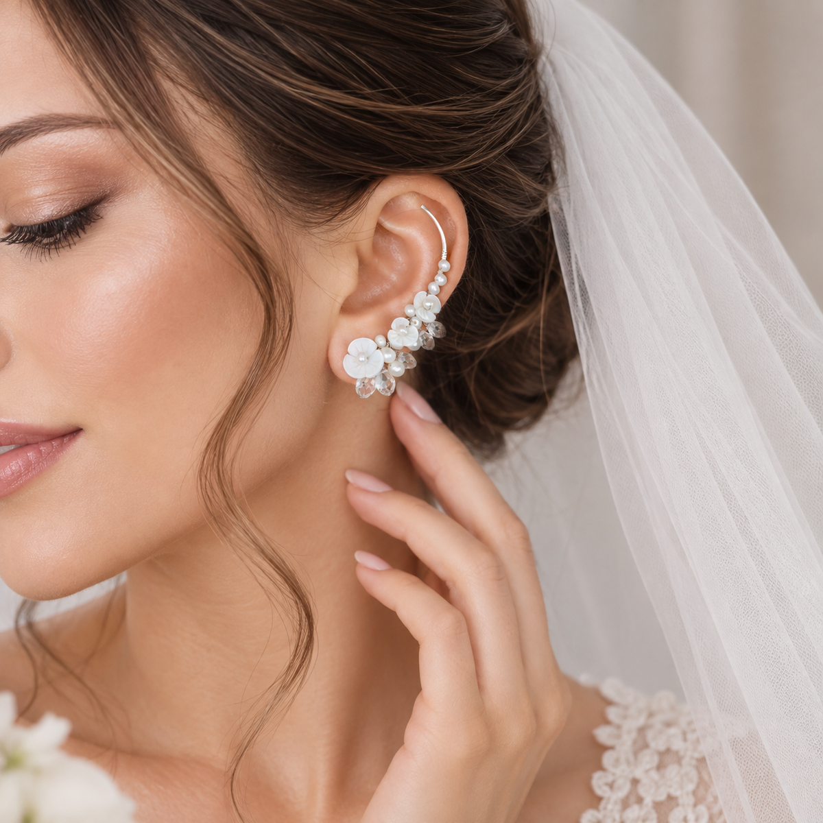 Bridal ear crawler worn with a formal updo and veil, decorated with genuine freshwater pearls, luminous flower shapes and clear crystal briolettes for a detailed wedding look.