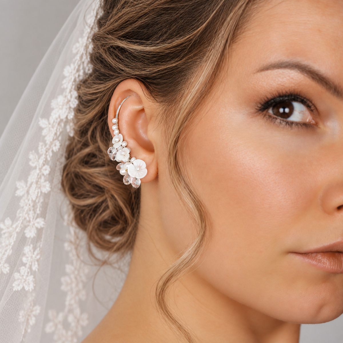 Bridal ear crawler worn with a formal updo and veil, decorated with genuine freshwater pearls, luminous flower shapes and clear crystal briolettes for a detailed wedding look.