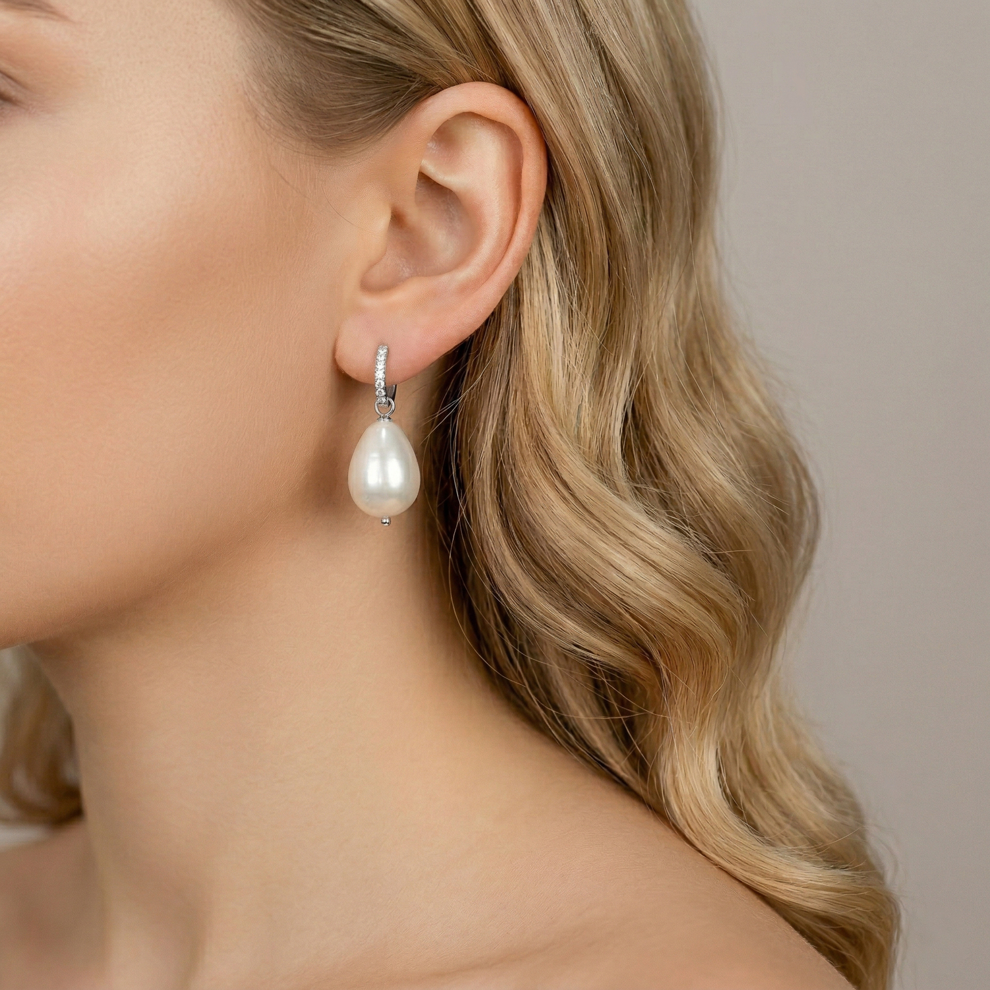 Close-up profile view of a model wearing a polished silver huggie hoop earring with clear pave diamonds and a large lustrous teardrop pearl drop, against a neutral background.