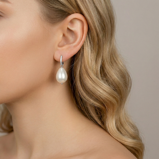 Close-up profile view of a model wearing a polished silver huggie hoop earring with clear pave diamonds and a large lustrous teardrop pearl drop, against a neutral background.