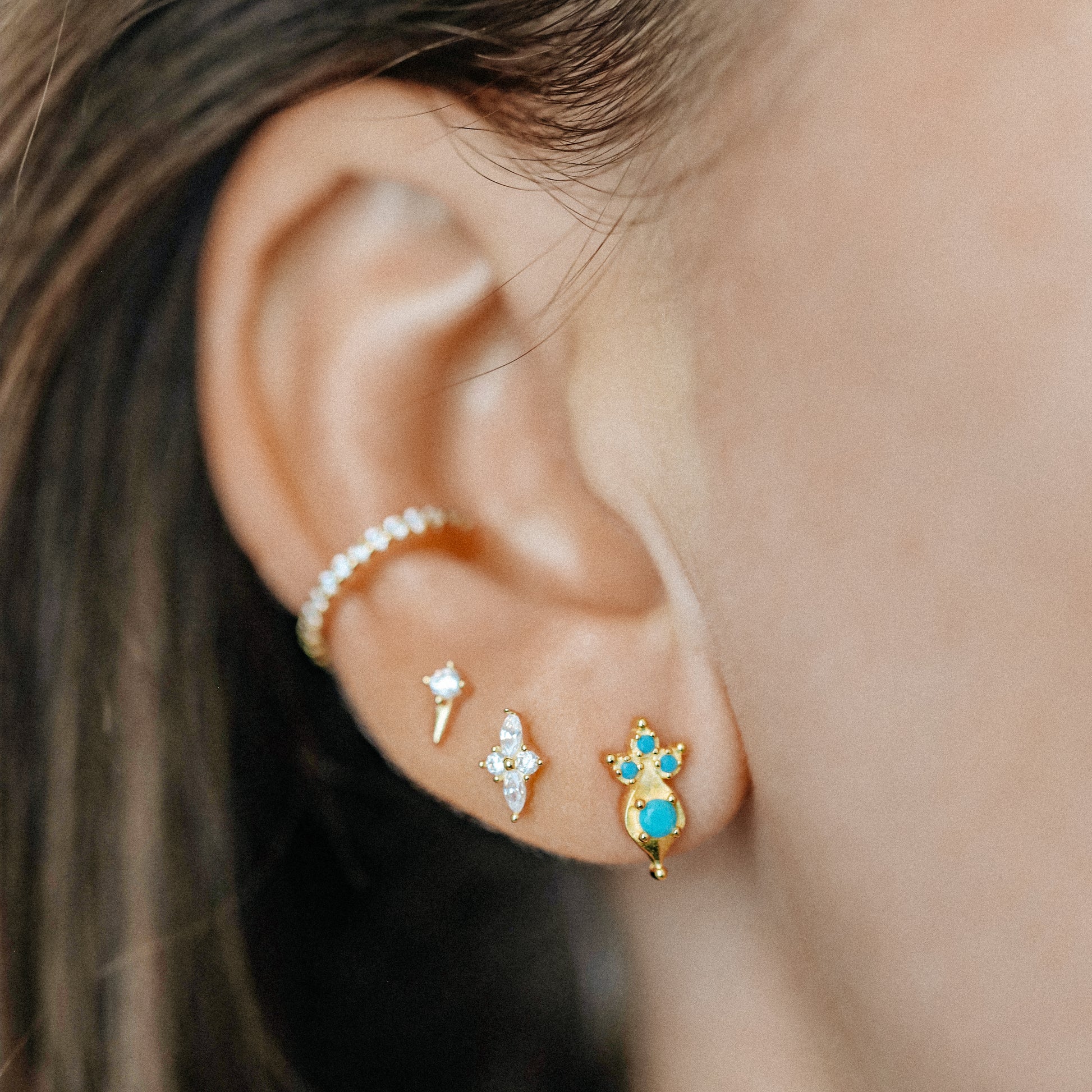 Tiny turquoise ear studs styled in multiple ear piercings