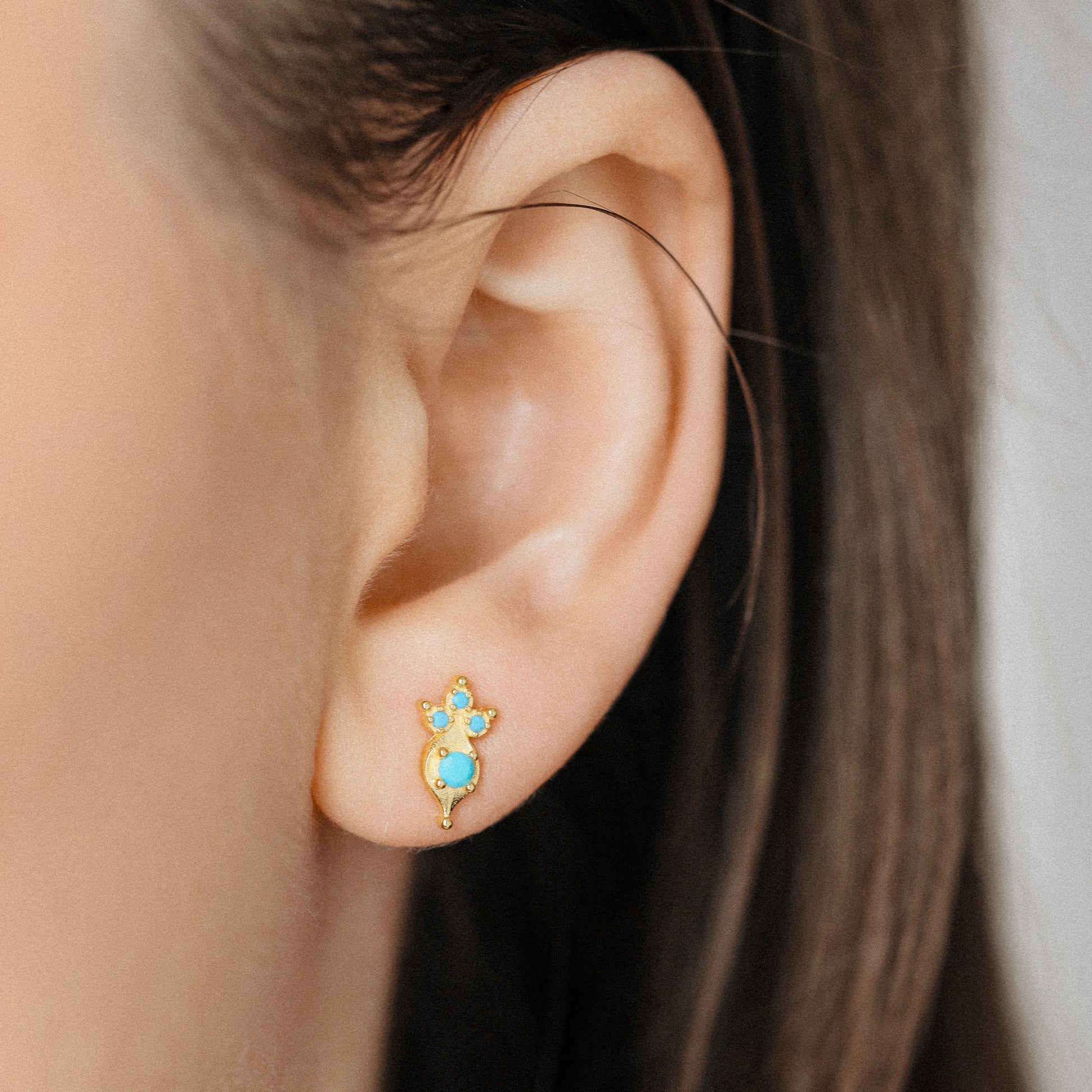 Tiny turquoise stud earrings in gold worn on ear close up