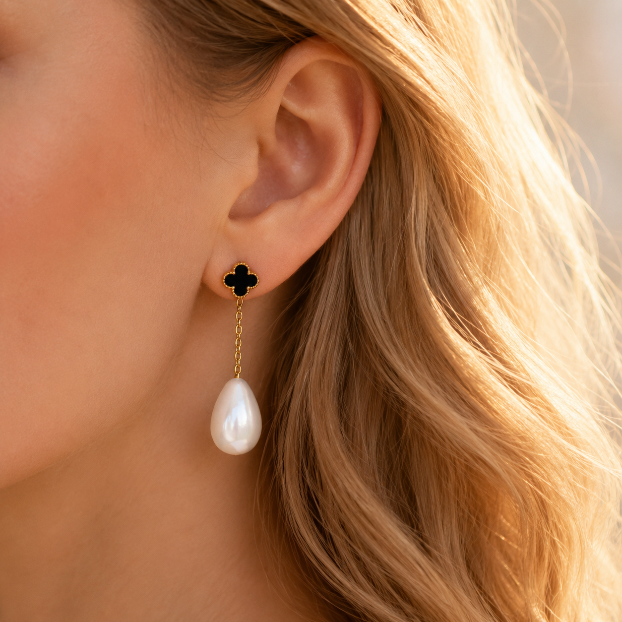 Black clover pearl drop earring worn on ear with long gold chain and teardrop pearl