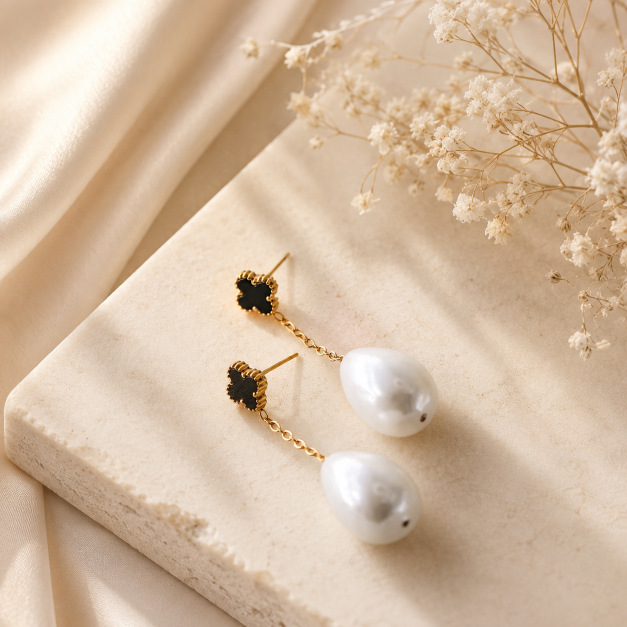 Black clover pearl drop earrings displayed on neutral fabric with gold chain detail