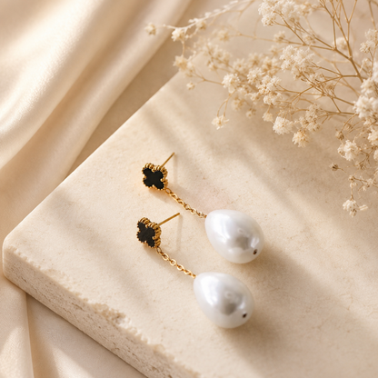 Black clover pearl drop earrings displayed on neutral fabric with gold chain detail