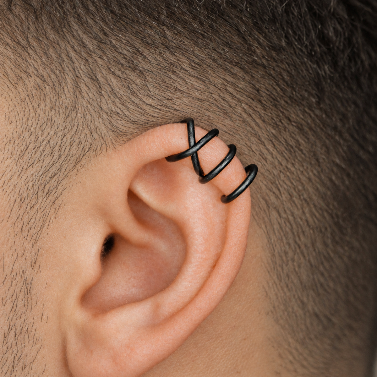 Close-up of a black Criss-Cross ear cuff positioned on the upper helix, showing the smooth rounded wire and layered wrap design.