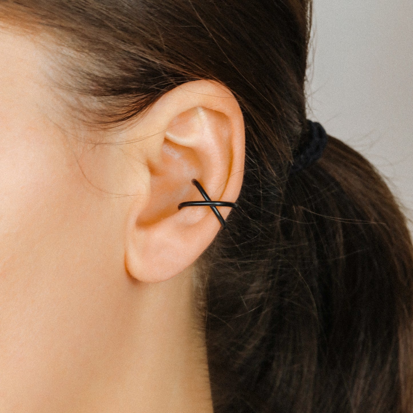Black criss cross ear cuff worn on the upper ear, featuring a bold no piercing conch ear cuff design.
