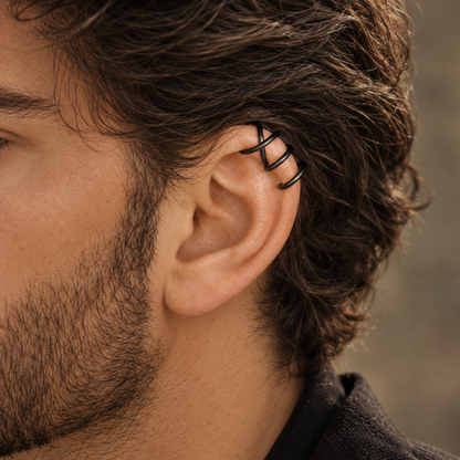 Black helix ear cuff worn by a man with a beard and longer hair, creating a minimal alternative jewelry look on the upper ear.