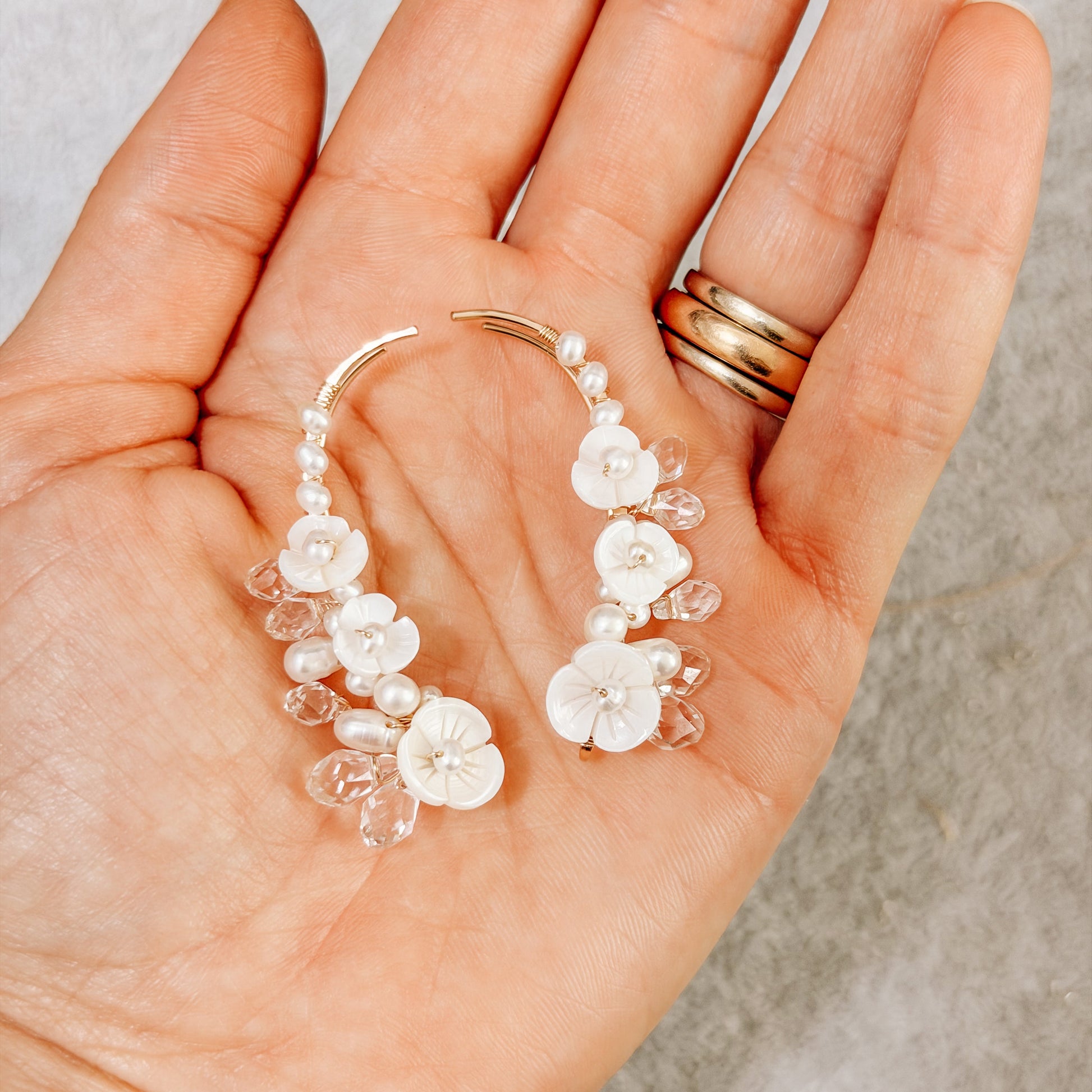 Hand holding floral pearl ear climbers to show their detailed handmade design